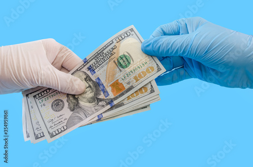 Isolated 2 female hands in medical gloves with a banknote of 100 dollars isolated on a blue background. The concept of corruption or quarantine, Covid 19.