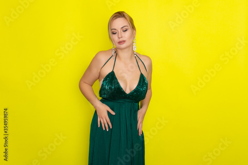 Blond woman wearing green evening dress over yellow background