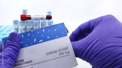 Doctor showing box of medicine for covid-19 treatment.Concept of covid stop medicine with blood tests tubes on the background.Cure for coronavirus,COVID-19 treatment.White with copy space photo