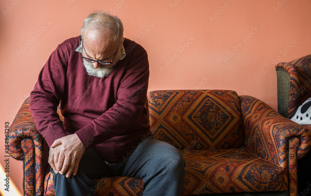 Old man suffering from pain in knee. Elderly senior man has rheumatism pain in his legs. Unhappy man in pain sitting on sofa at home, feel sick. Aged sad man with knee pain. Rheumatoid disease concept Old man suffering from pain in knee. Elderly senior man has rheumatism pain in his legs. Unhappy man in pain sitting on sofa at home, feel sick. Aged sad man with knee pain. Rheumatoid disease concept