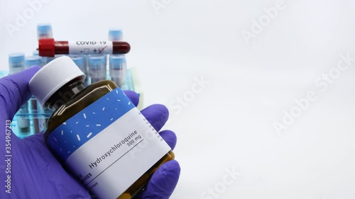 Dubai-UAE-Circa 2020:Doctor showing bottle of medicine for covid-19 treatment.Concept of Hydroxychloroquine medicine with blood tests tubes on the background.Cure for coronavirus,COVID-19 treatment. photo
