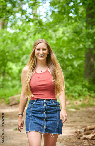 Beautiful young blonde woman walking in woods wearing orange tank top and denim skirt - outdoors