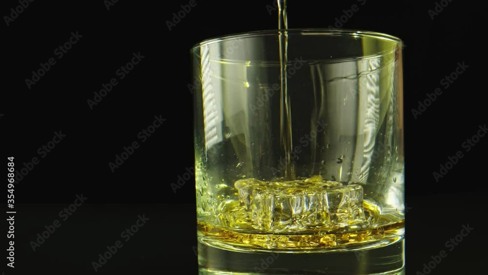Macro shot in slow motion of a drink being poured on a glass. Background is black. Macro shot in slow motion of a drink being poured on a glass. Background is black.