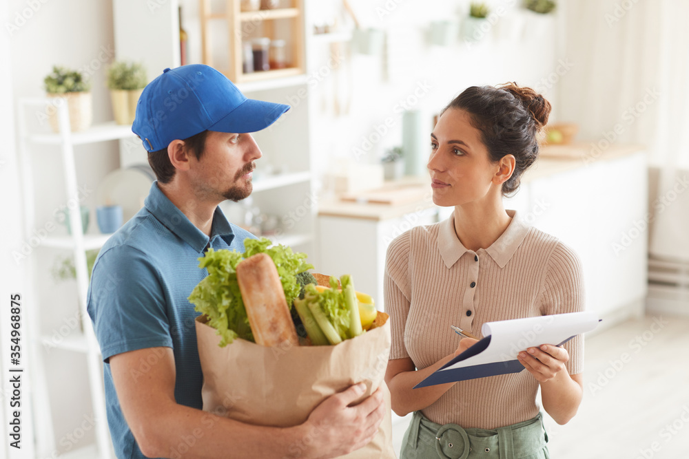 Young woman signing the contract for delivery while delivery man holding the products Young woman signing the contract for delivery while delivery man holding the products