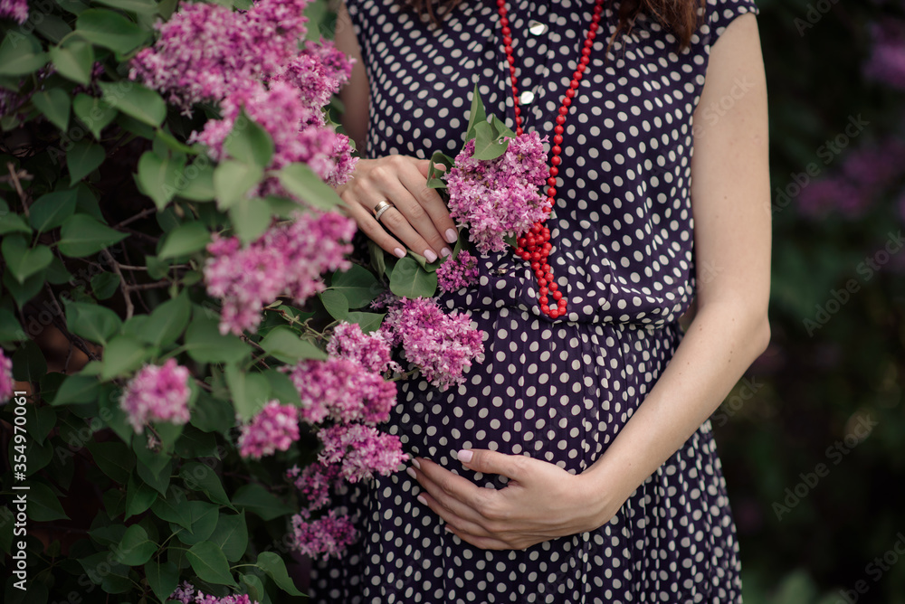 Pregnant Woman Belly. Pregnancy Concept. Over green nature blurred Background. Pregnant tummy close up. Expectant female touching tummy outdoor in spring park, holding bunch of dandelions. Sun light