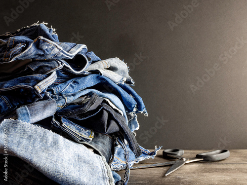 Pile of old blue jeans ready for recycling in the circular economy. Scissors on a wooden table, dark background. Room for text. 
