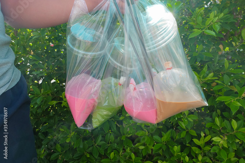 People carrying Sweet water seller is green nectar, pink nectar and coffee into clear bag with clear plastic glass from delivery ,background is green leaves, concept seller water delivery photo