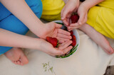 Red strawberry in the hands of children. Children's friendship, summer warm day.