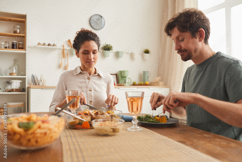 Young couple sitting at the table and enjoying dinner together in domestic kitchen Young couple sitting at the table and enjoying dinner together in domestic kitchen