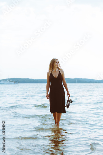 woman in black light dress walking barefoot by sea beach