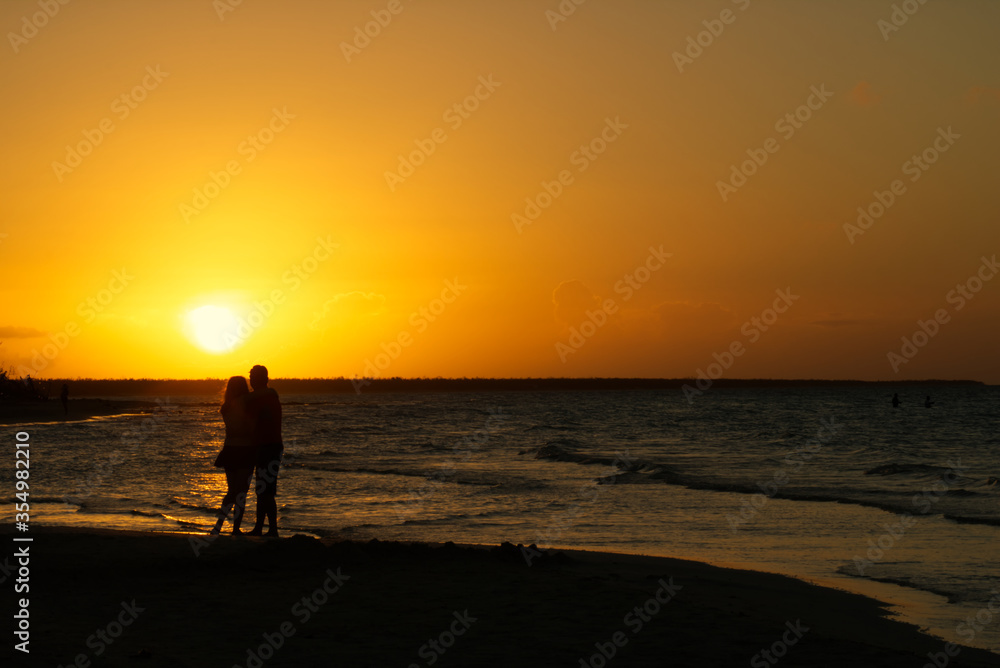 Couple hugging each other in front of a golden sunset on the beach