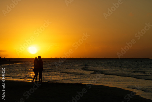Couple hugging each other in front of a golden sunset on the beach