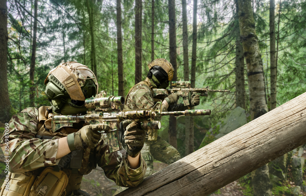 Soldiers in multicam camouflage aiming in forest.