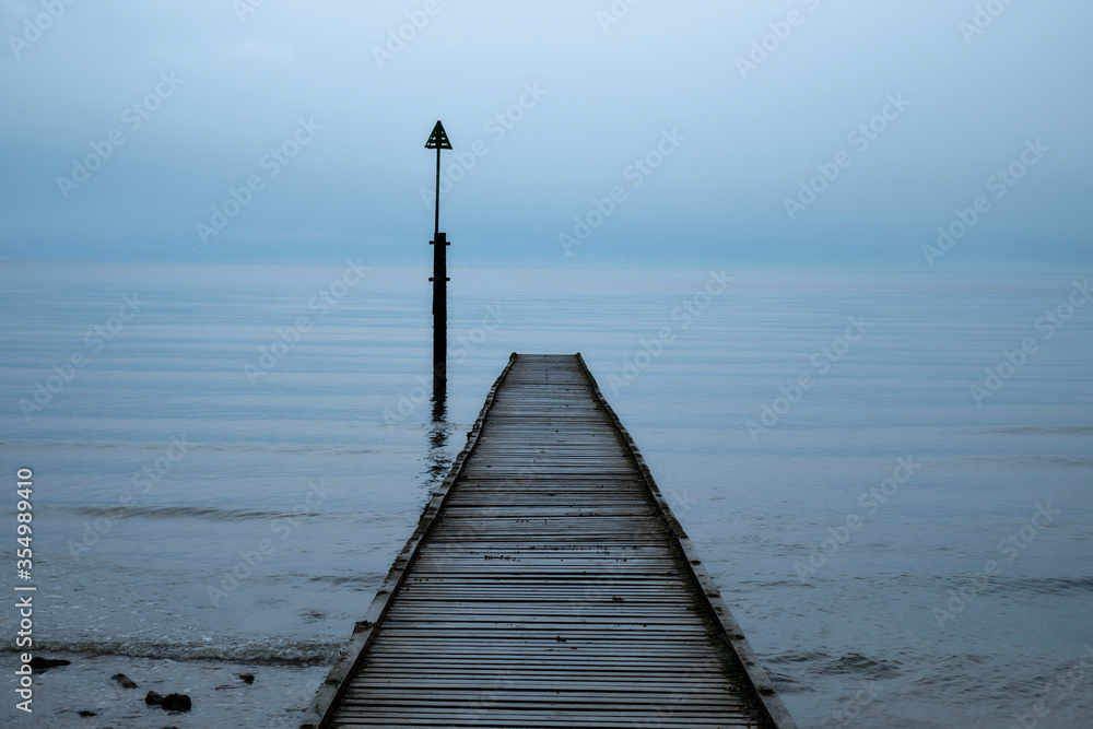Old wooden single pier leading into a foggy ocean with little variation from sky to water