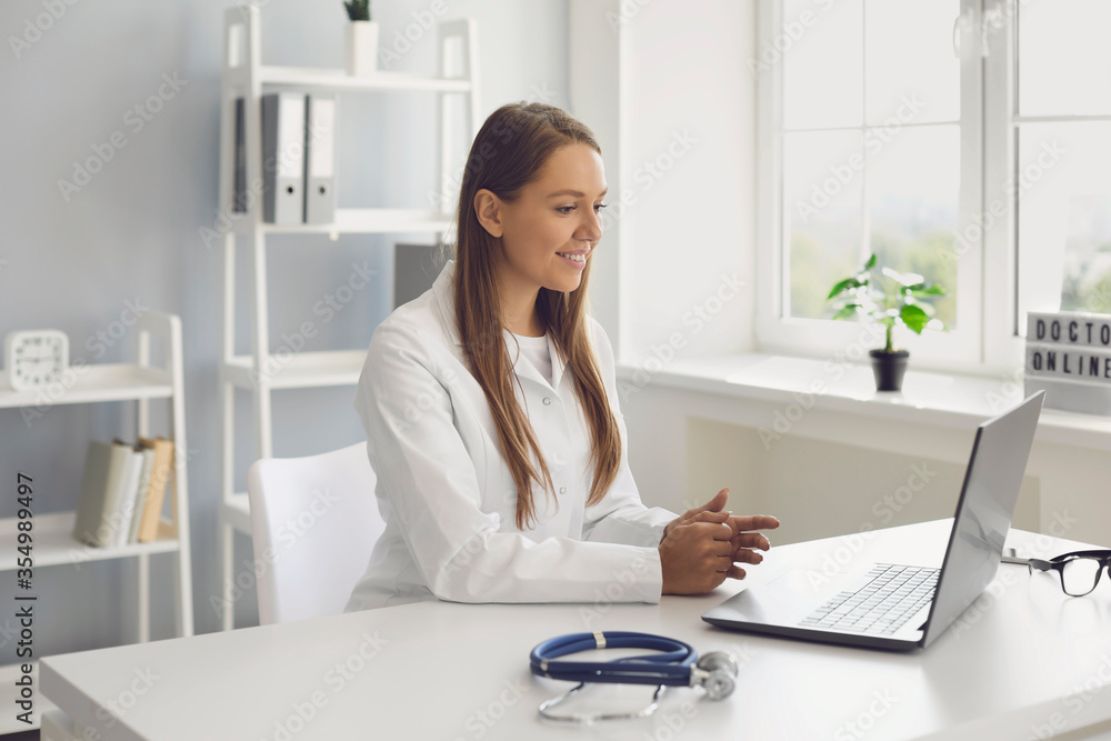 Young female doctor consulting patient online, using laptop computer at her office. GP making video call to sick client Young female doctor consulting patient online, using laptop computer at her office. GP making video call to sick client