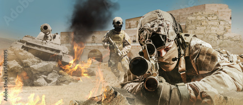 Żołnierz kładący i celujący karabin na pustynnym polu bitwy z czołgami i żołnierzami atakującymi.