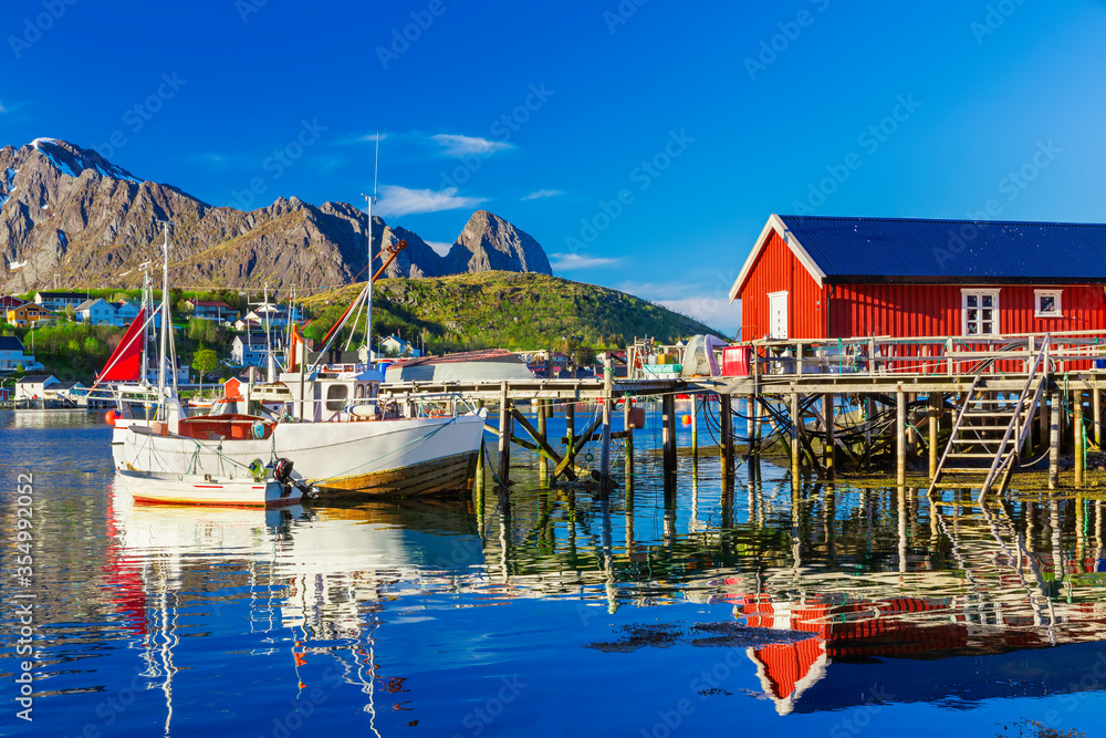Fishing boats in Reine Village, Lofoten Islands,  Norway.  The Typical Norwegian fishing village of Reine under midnight sun,  with the typical red rorbu houses.  Mountain In Background