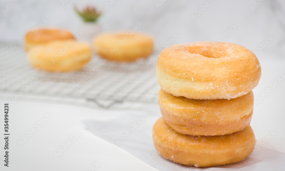 Homemade deep fried donuts in stack with sugar standing on crumpled paper wooden with marble table.
