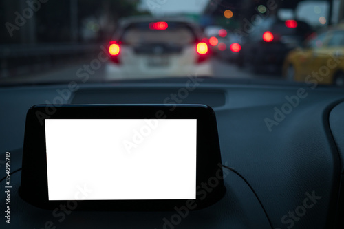 Display of GPS or navigator device in a holder in car with blur background of traffic jams in the evening. Mockup white empty screen for text, copy space