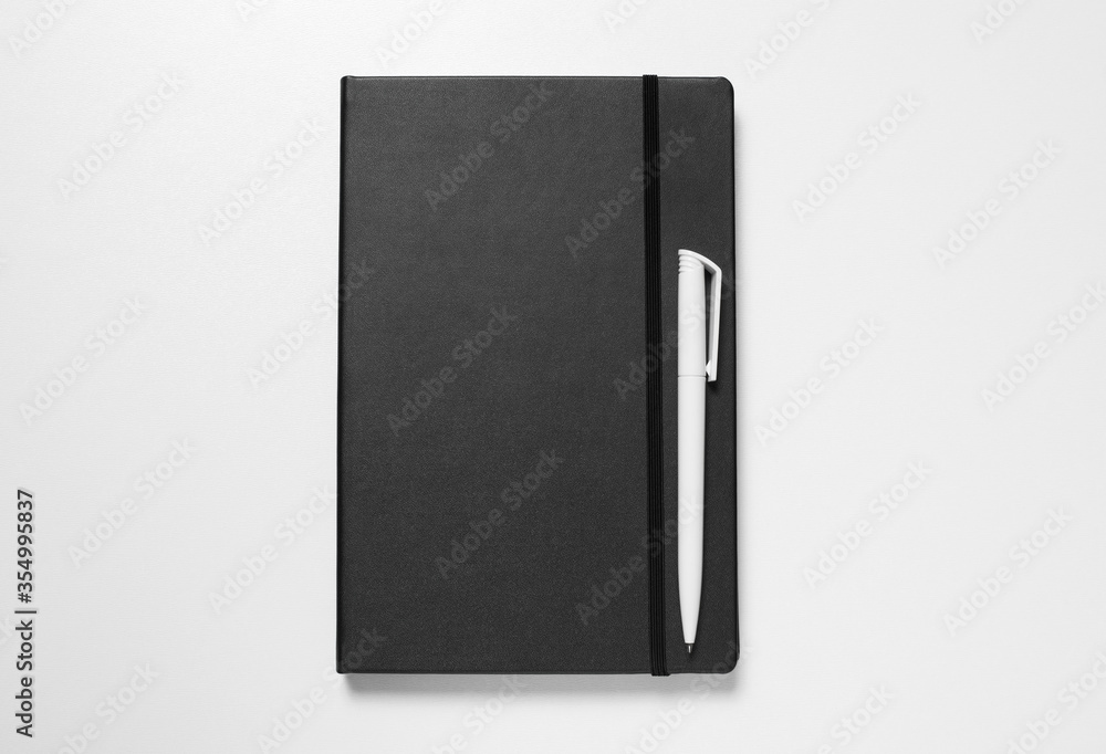 The white pen lies on black paper notebook. Light background. The white pen lies on black paper notebook. Light background.