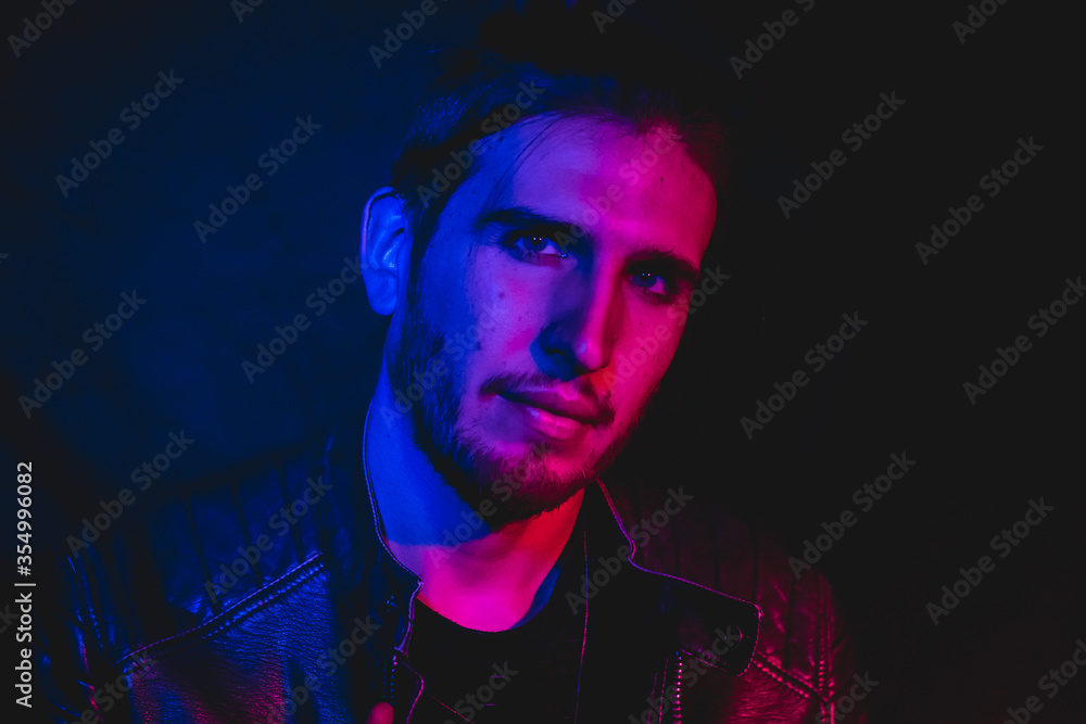 Man in his 30s posing to the camera with blue and red lighting, close up portrait 