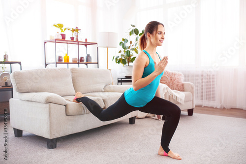 Young fitness woman doing lunges exercise is using furniture for workout at home. Sports training in living room. Copy space