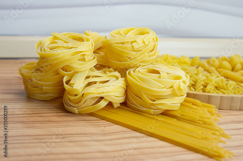 Pasta nests spaghetti scallops linguini penne tagliatelle fusilli spirals on a blackboard and wooden background.