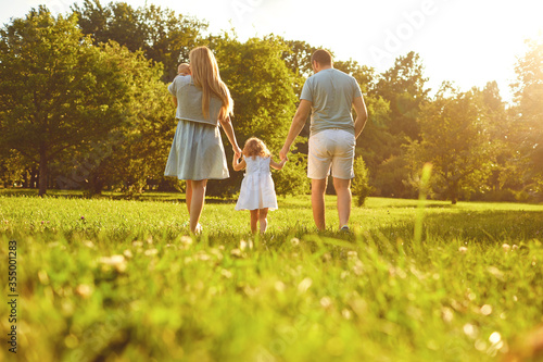 Happy family walking on the grass in the summer park. Mother father and children playing in nature. Children Protection Day.