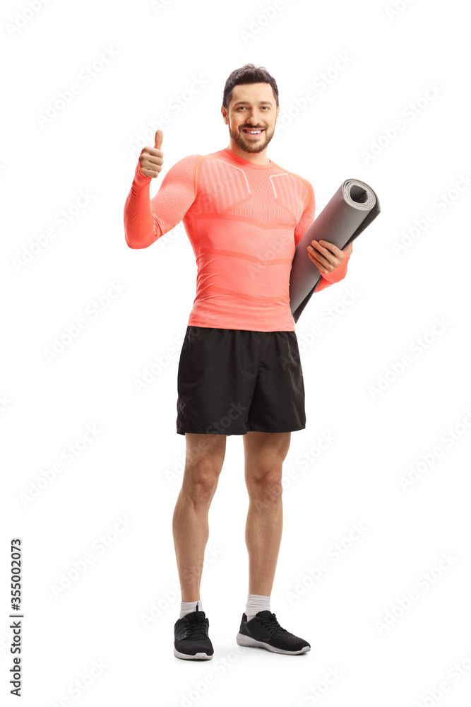 Fit man in sportswear holding an exercise mat and showing thumbs up Fit man in sportswear holding an exercise mat and showing thumbs up