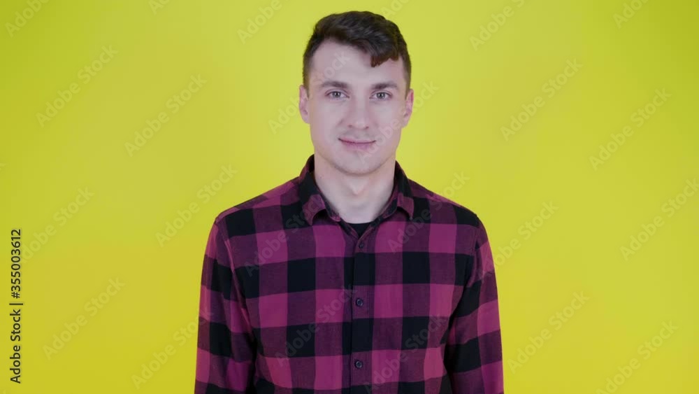 Sexy man in a pink plaid shirt flirts kissing the air and smiles on a yellow background with copy space. Place for text or product. 4K slow motion footage Sexy man in a pink plaid shirt flirts kissing the air and smiles on a yellow background with copy space. Place for text or product. 4K slow motion footage