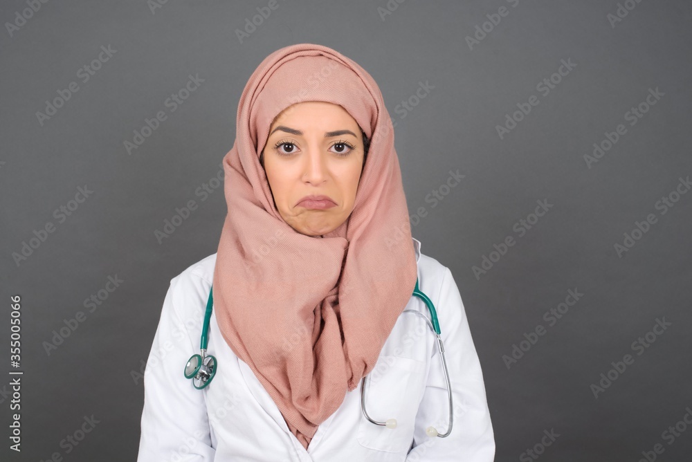 Beautiful face of sad doctor woman crying desperate and depressed with tears on her eyes suffering pain and depression isolated on grey background in sadness facial expression and emotion concept. Beautiful face of sad doctor woman crying desperate and depressed with tears on her eyes suffering pain and depression isolated on grey background in sadness facial expression and emotion concept.
