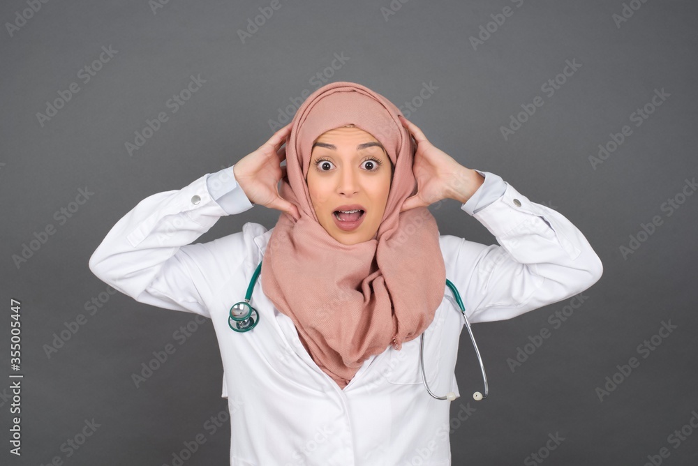 Excited overjoyed muslim doctor woman screams after receiving good news, keeps hands on head, can't believe it. Excited overjoyed muslim doctor woman screams after receiving good news, keeps hands on head, can't believe it.