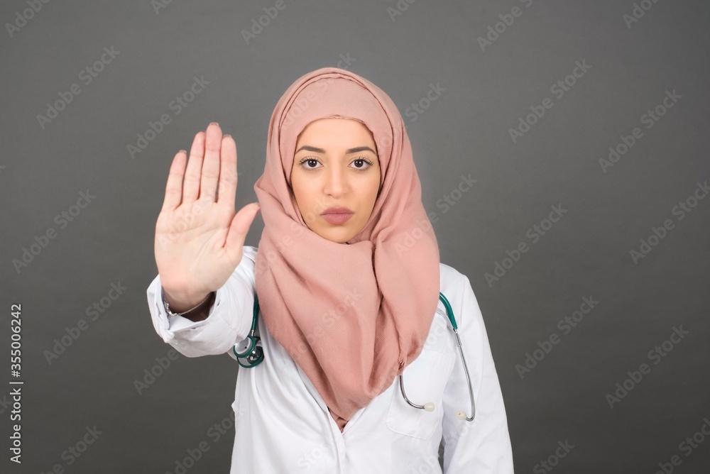 Young beautiful caucasian doctor woman doing stop gesture with palm of the hand. Warning expression with negative and serious gesture on the face isolated over gray background. Young beautiful caucasian doctor woman doing stop gesture with palm of the hand. Warning expression with negative and serious gesture on the face isolated over gray background.