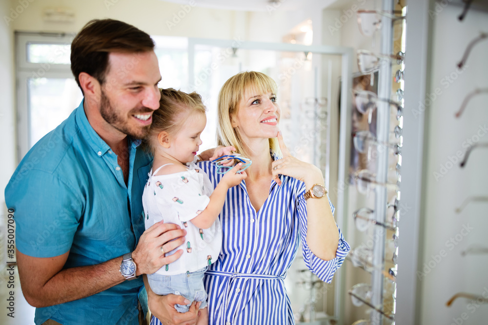 Happy mother and father choosing eyeglasses frame with their daughter in optical store Happy mother and father choosing eyeglasses frame with their daughter in optical store