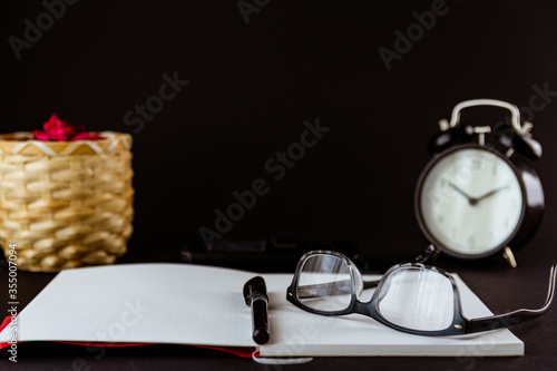Still life con reloj antiguo sobre escritorio con libros, reloj despertador, gafas y fondo negro o blanco