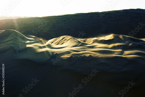 The wind blows thin sand from crest of dune photo