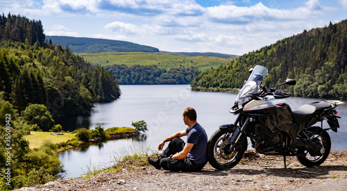 Adventure motorcycle and biker man traveling, sitting and watching landscape with lake and mountains, freedom travel lifestyle in Wales UK photo