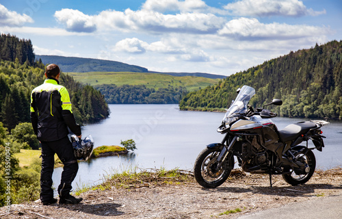 Adventure motorcycle and biker man traveling, standing and watching landscape with lake and mountains, freedom travel lifestyle in Wales UK