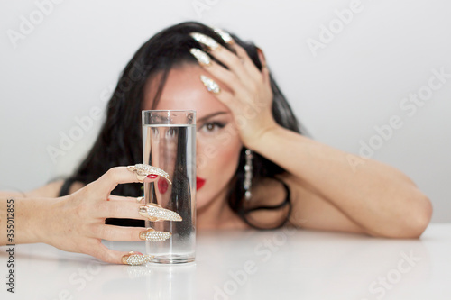 Beautiful woman profesional makeup red lips red nails reflected in a glass of water