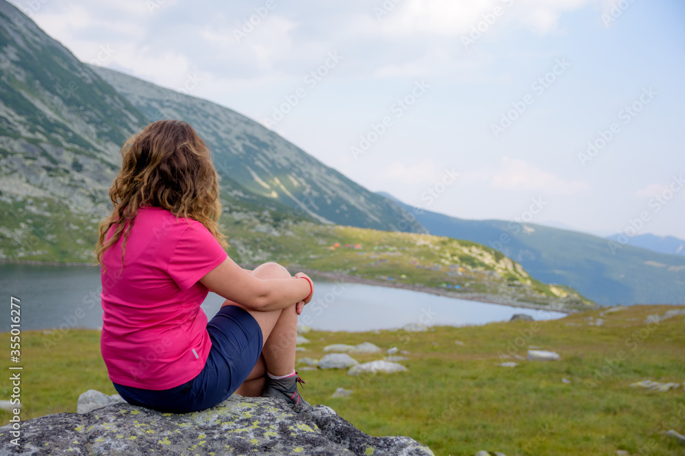 Young girl with colored shirt and wavy hair looking over glaciar lake in Carpathians mountains in Romania