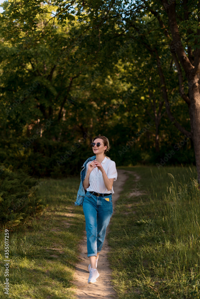 Joyful young woman in fashionable sunglasses walking in nature on a beautiful day Joyful young woman in fashionable sunglasses walking in nature on a beautiful day