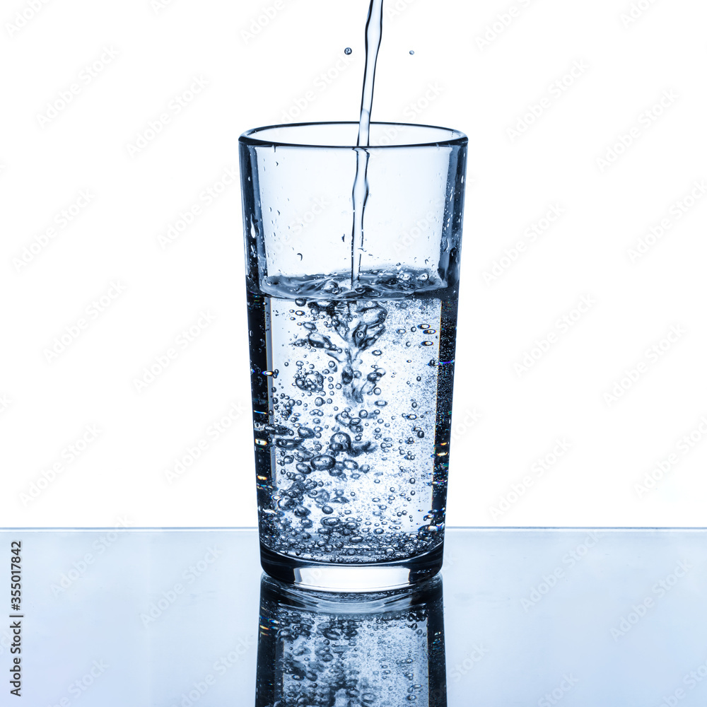 A stream of clean drinking water is poured into a glass cup A stream of clean drinking water is poured into a glass cup