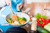 Young housewife holding pan with various vegetables and mixing spoon. Vegetarian food cooking.