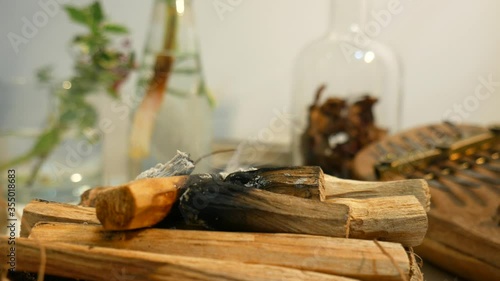 Smoking Palo Santo Centered in Foreground with Dried Jasmine Flowers in Glass used for Meditation Energy Work Yoga Reiki Healing Other Crystals and Plants in Background in 4k