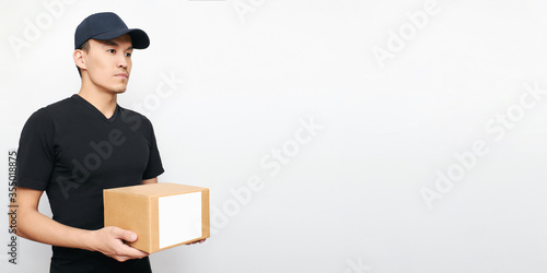 An Asian courier holds a box with copy space on a white background. Concept of a business service for food delivery during quarantine and the COVID-19 virus