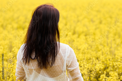 Young woman in a white dress standing in a rapeseed field. Blooming yellow flowers with copy space