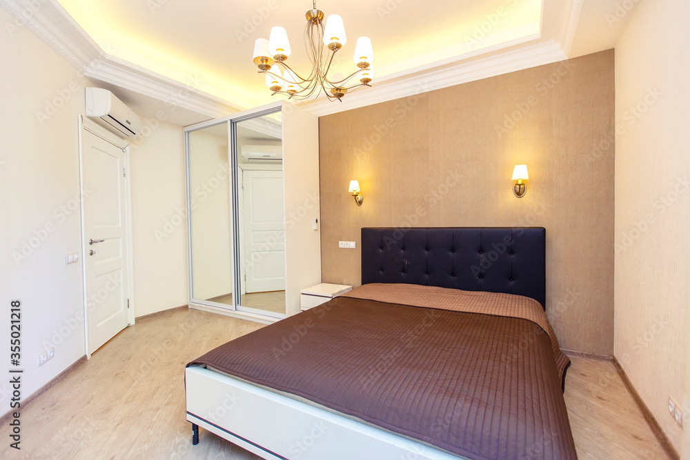 A bright Bedroom with a large double bed with a brown bedspread. Built-in wardrobe, nightstand, ceiling with lighting. Brown Wallpaper inserts A bright Bedroom with a large double bed with a brown bedspread. Built-in wardrobe, nightstand, ceiling with lighting. Brown Wallpaper inserts
