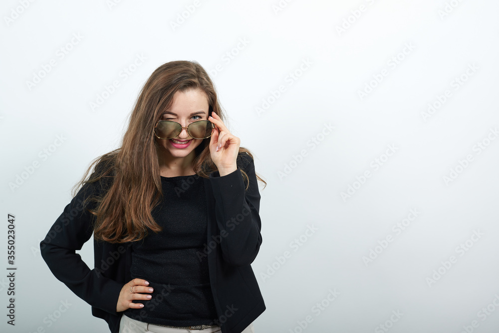 Young attractive brunette woman in a black t-shirt and sweater on white background, stylish female in sunglasses winks. Fashionable, modern people Young attractive brunette woman in a black t-shirt and sweater on white background, stylish female in sunglasses winks. Fashionable, modern people