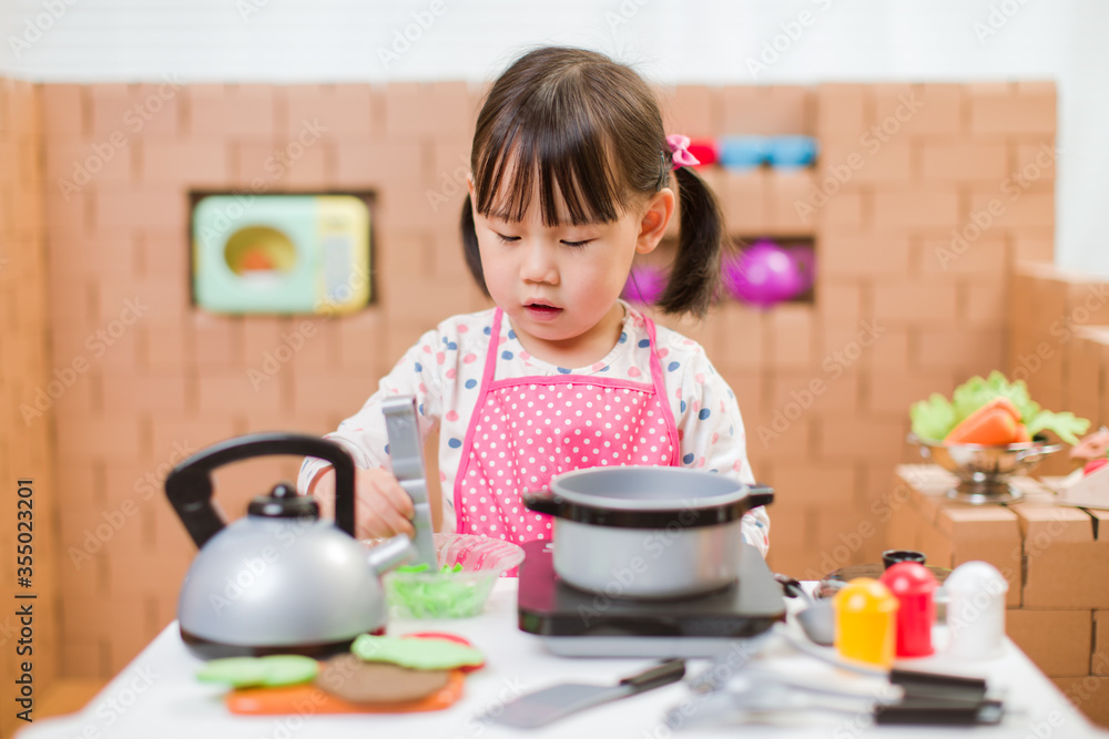 toddler girl pretend play food preparing role against cardboard blocks kitchen background toddler girl pretend play food preparing role against cardboard blocks kitchen background