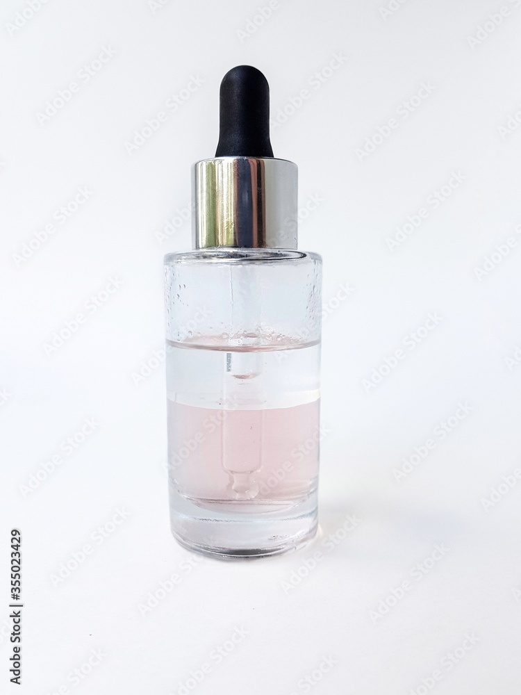 Cosmetic glass bottle with liquid inside and pipette, black rubber cap on a white background close-up. Cosmetic glass bottle with liquid inside and pipette, black rubber cap on a white background close-up.